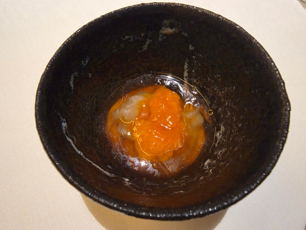 A black ceramic bowl containing a mixture of bright orange egg yolk and translucent seafood.