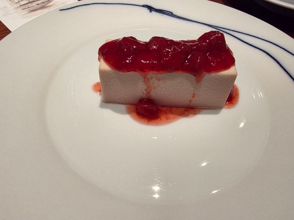 A rectangular dessert topped with red fruit sauce, served on a white plate.