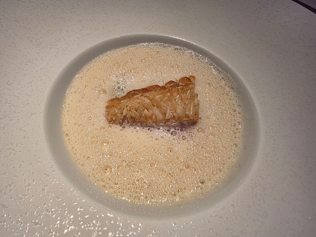 A piece of crispy fish fillet resting on a bed of frothy cream sauce in a white bowl.