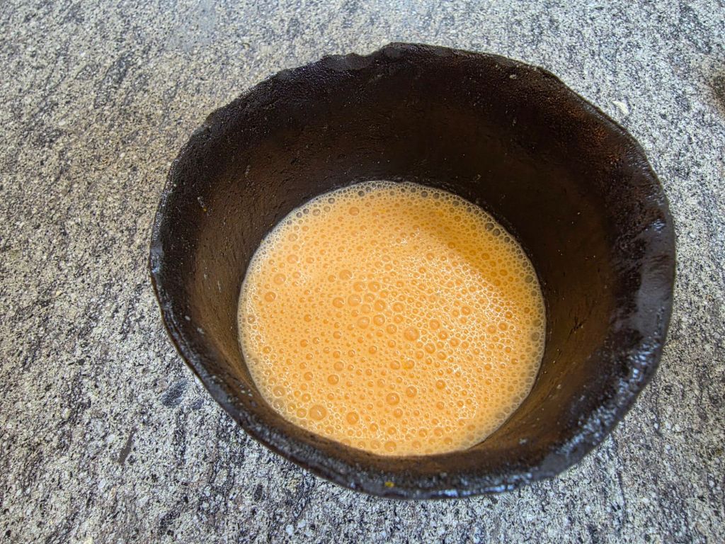 A round black bowl filled with frothy orange liquid, placed on a textured gray surface.