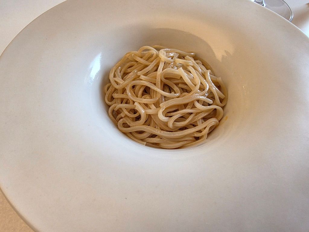 A close-up of cooked spaghetti noodles served in a white bowl.