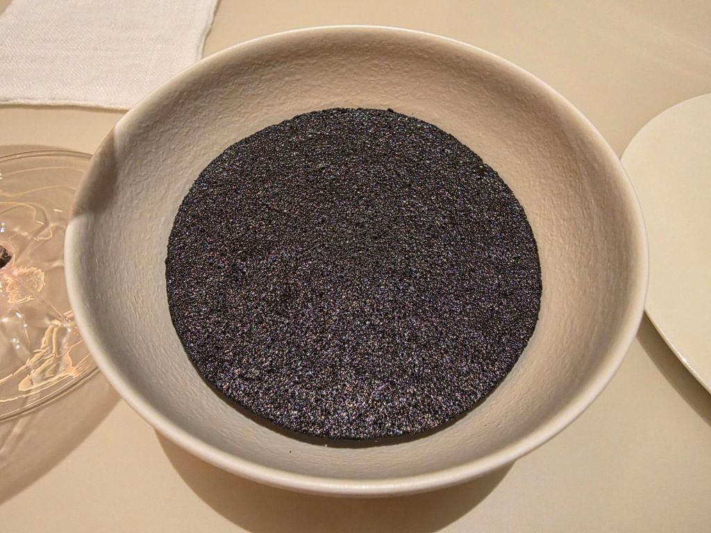 A round, shallow bowl containing a smooth, dark textured substance resembling a fine powder or paste.