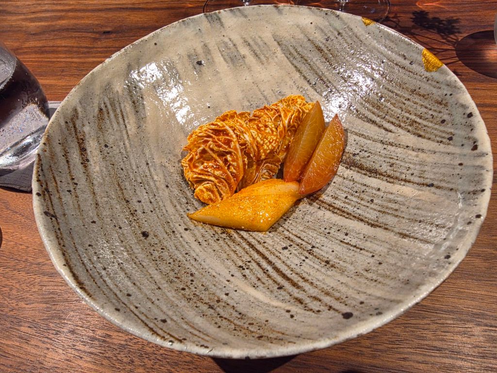 A textured ceramic plate with a serving of garnished food, featuring crispy elements and sliced fruits arranged artfully.