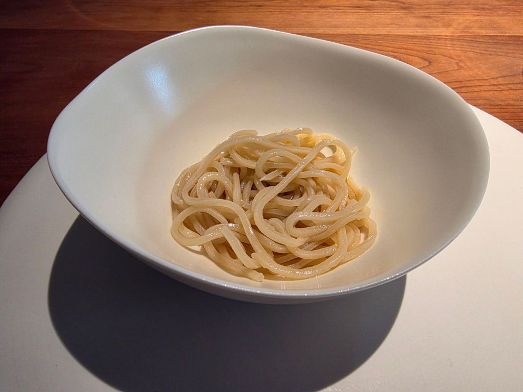 A serving of plain cooked spaghetti noodles in a white bowl on a wooden surface.