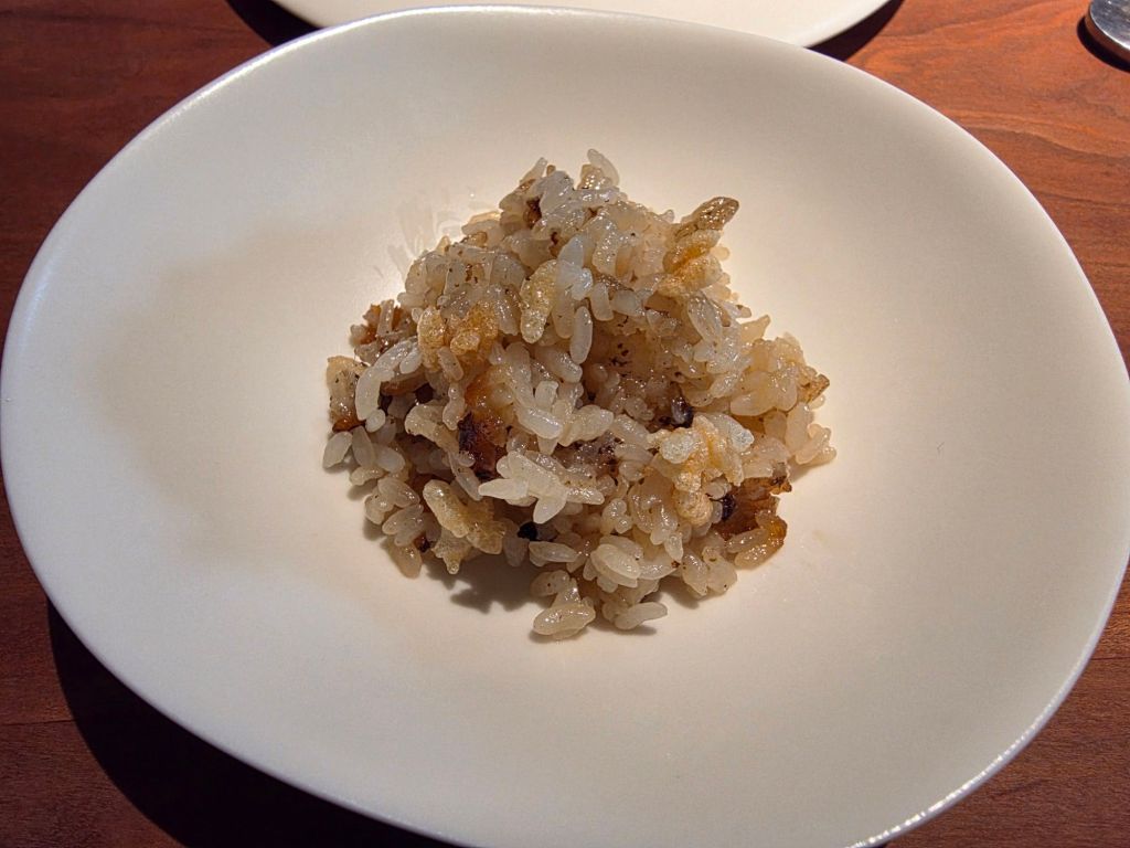 A serving of cooked rice with a slightly crispy texture, presented in a white bowl on a wooden table.