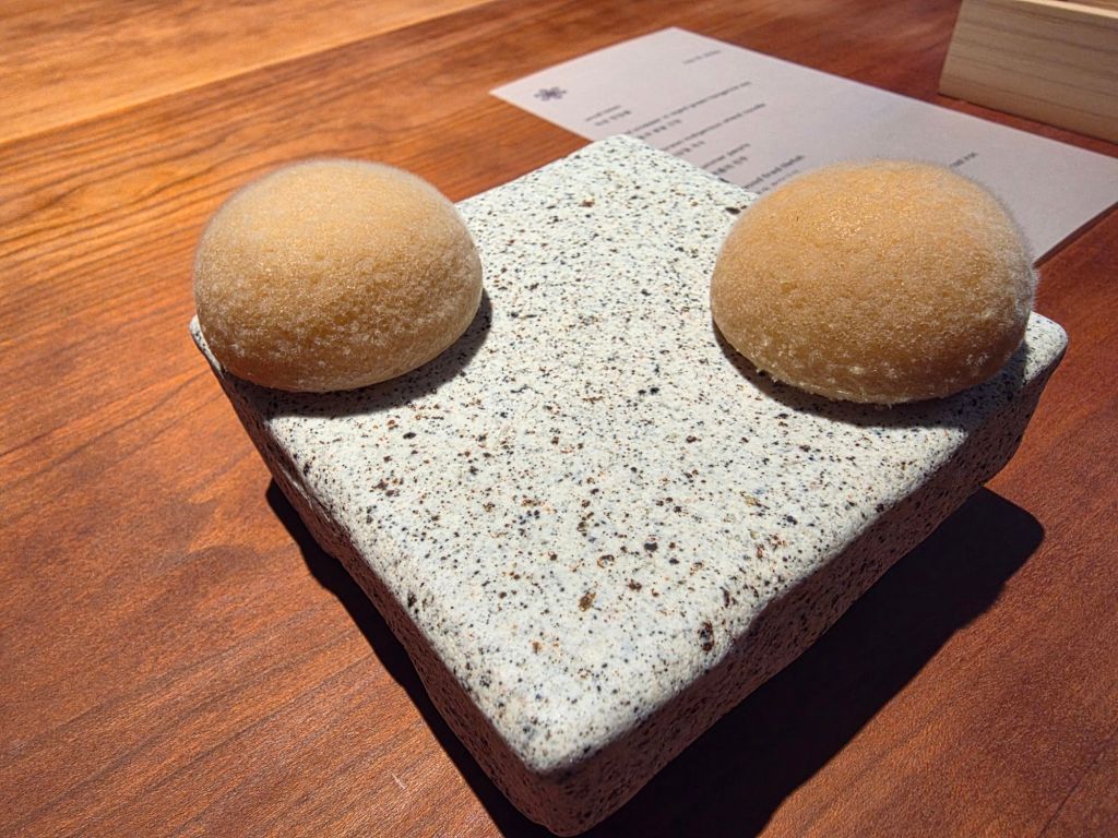 Two round, soft buns placed on a textured stone serving plate, set against a wooden tabletop.